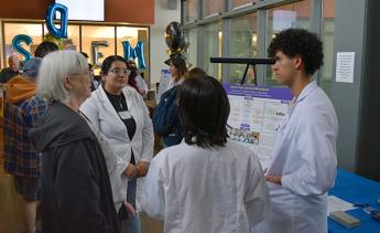Three biotechnology students talking to an older woman about their research presentation