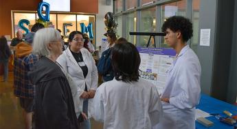 Three biotechnology students talking to an older woman about their research presentation
