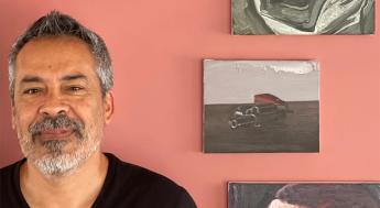 Photo portrait of Salomon Huerta standing in front of a red wall that displays a selection of his work