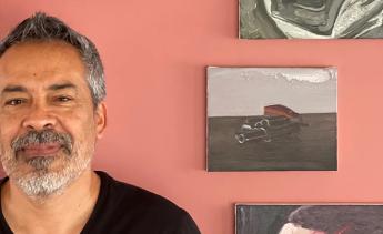 Photo portrait of Salomon Huerta standing in front of a red wall that displays a selection of his work