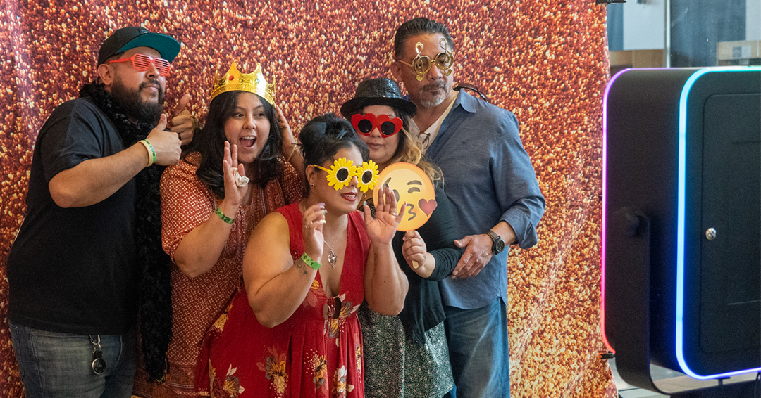 A group of attendees preparing to take a photo wearing silly hats and glasses in the photo booth at the San Fernando Valley Food & Wine Festival