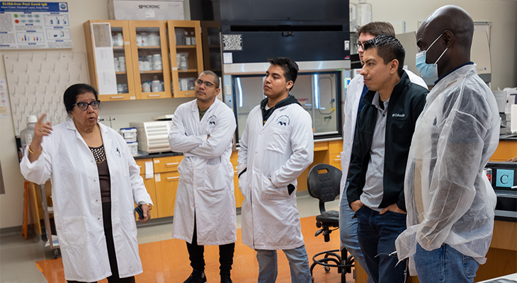 Students in lab coats standing and listening to an instructor