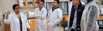 Students in lab coats standing and listening to an instructor